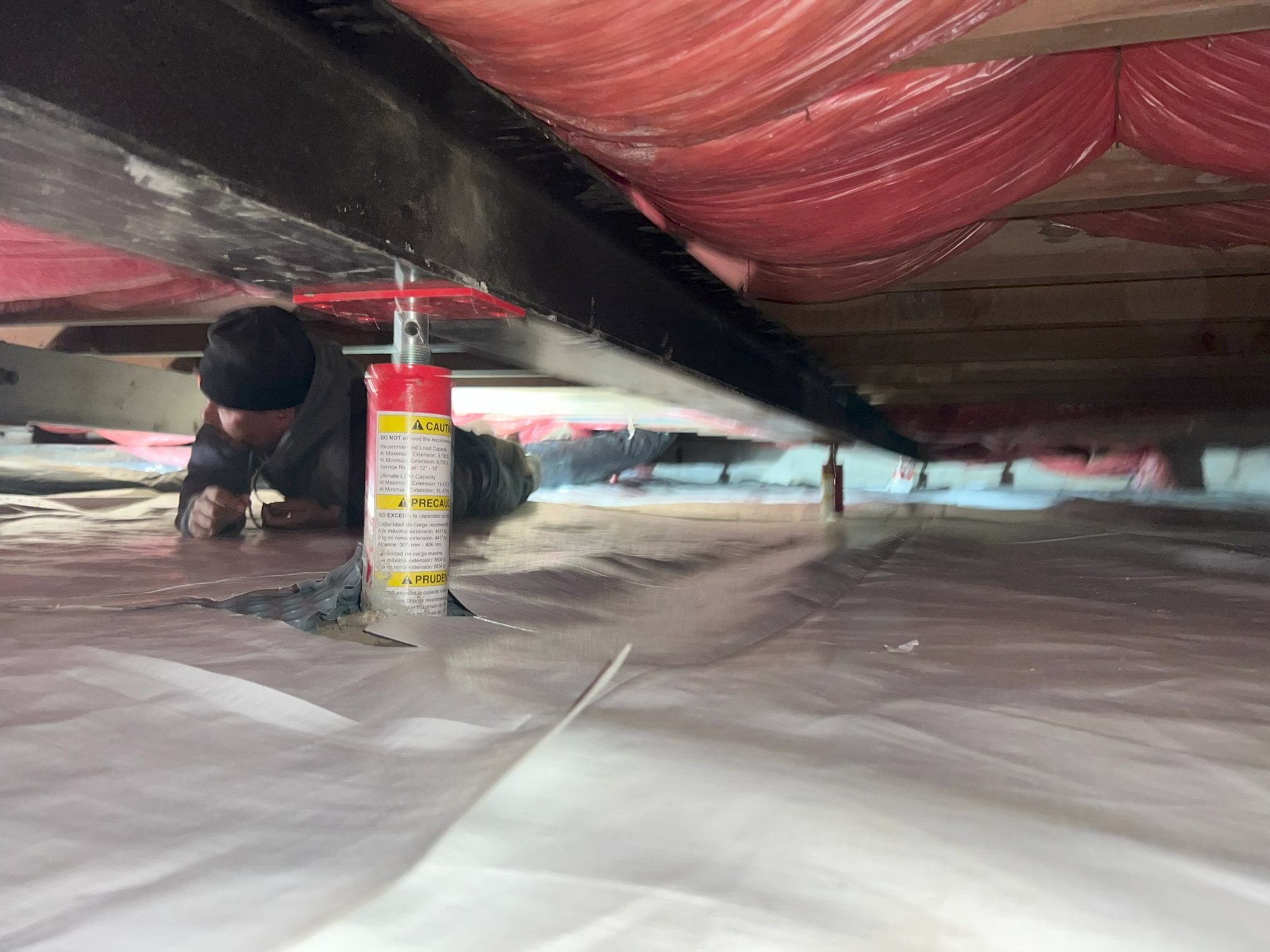 Basement foundation wall reinforced with painted white steel I-beams and white wall vapor barrier